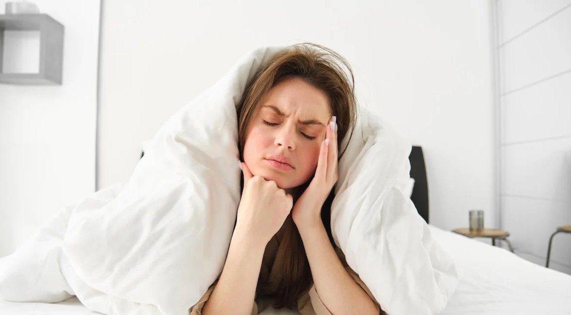 Restless woman holding painful jaw in bed before finding sleep relief after wisdom teeth removal in Sydney